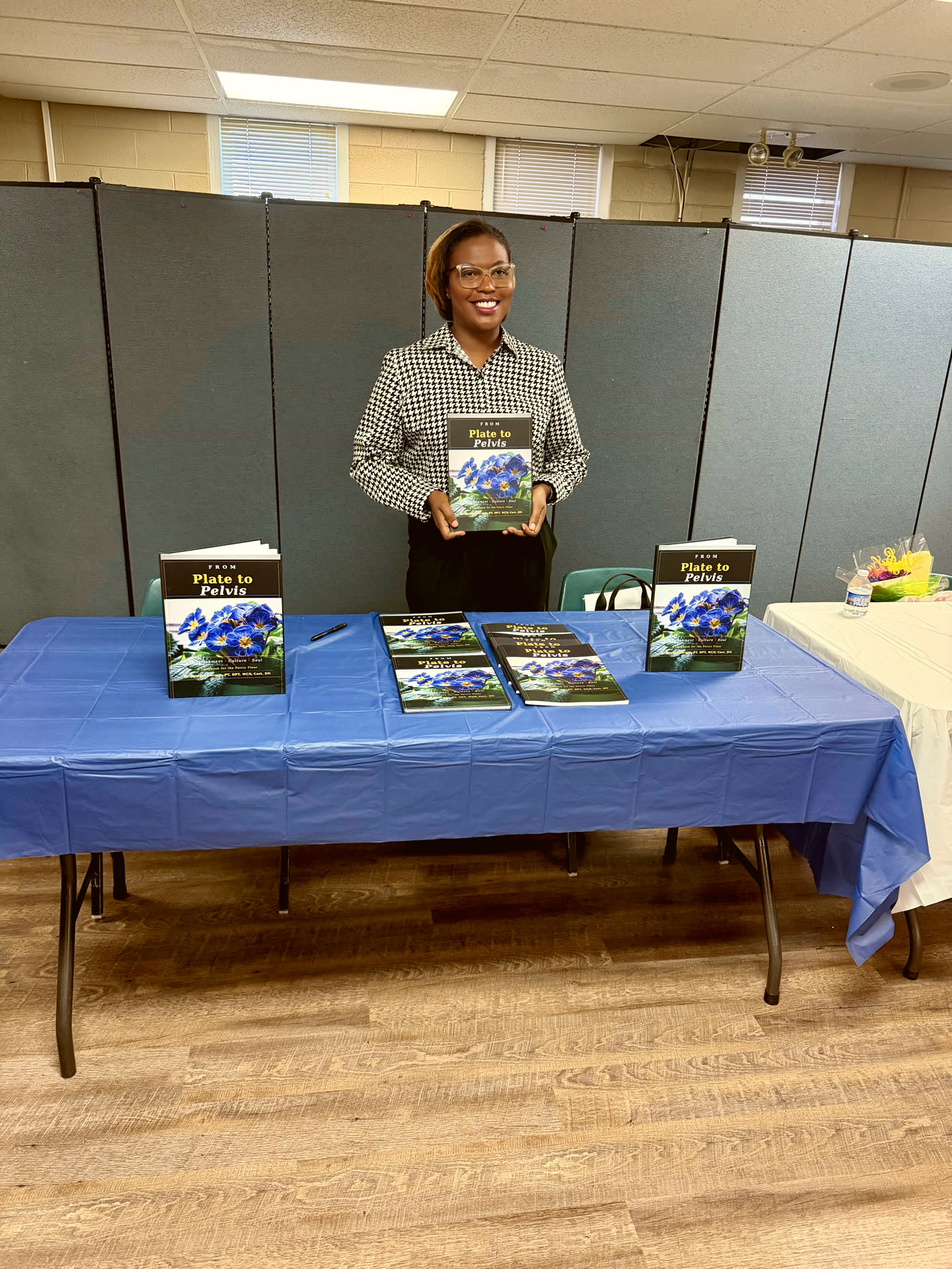 Dr. Kendra Garrett at a From Plate to Pelvis book signing table with copies of the cookbook